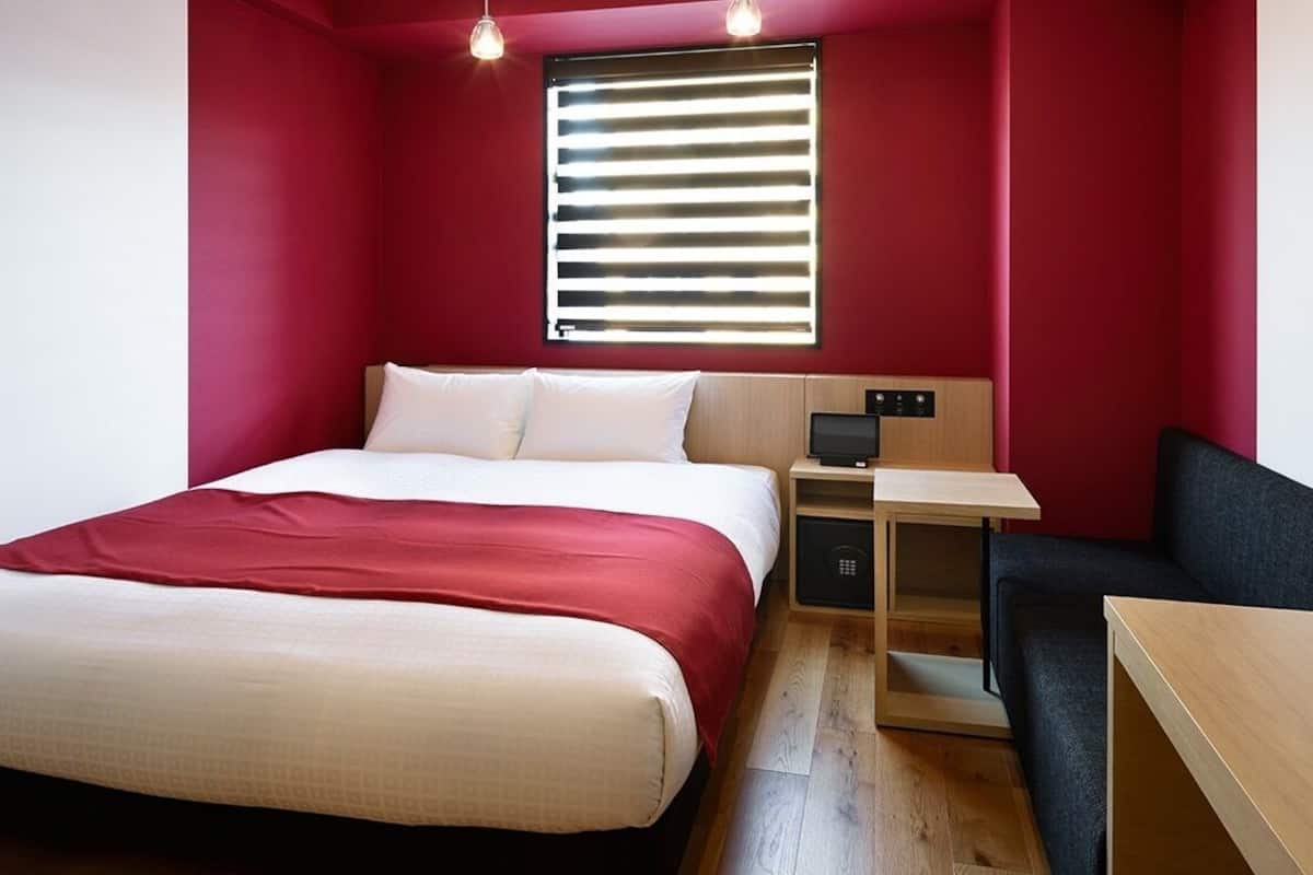 A bedroom with a bed, a desk, a chair, and a window with blinds.