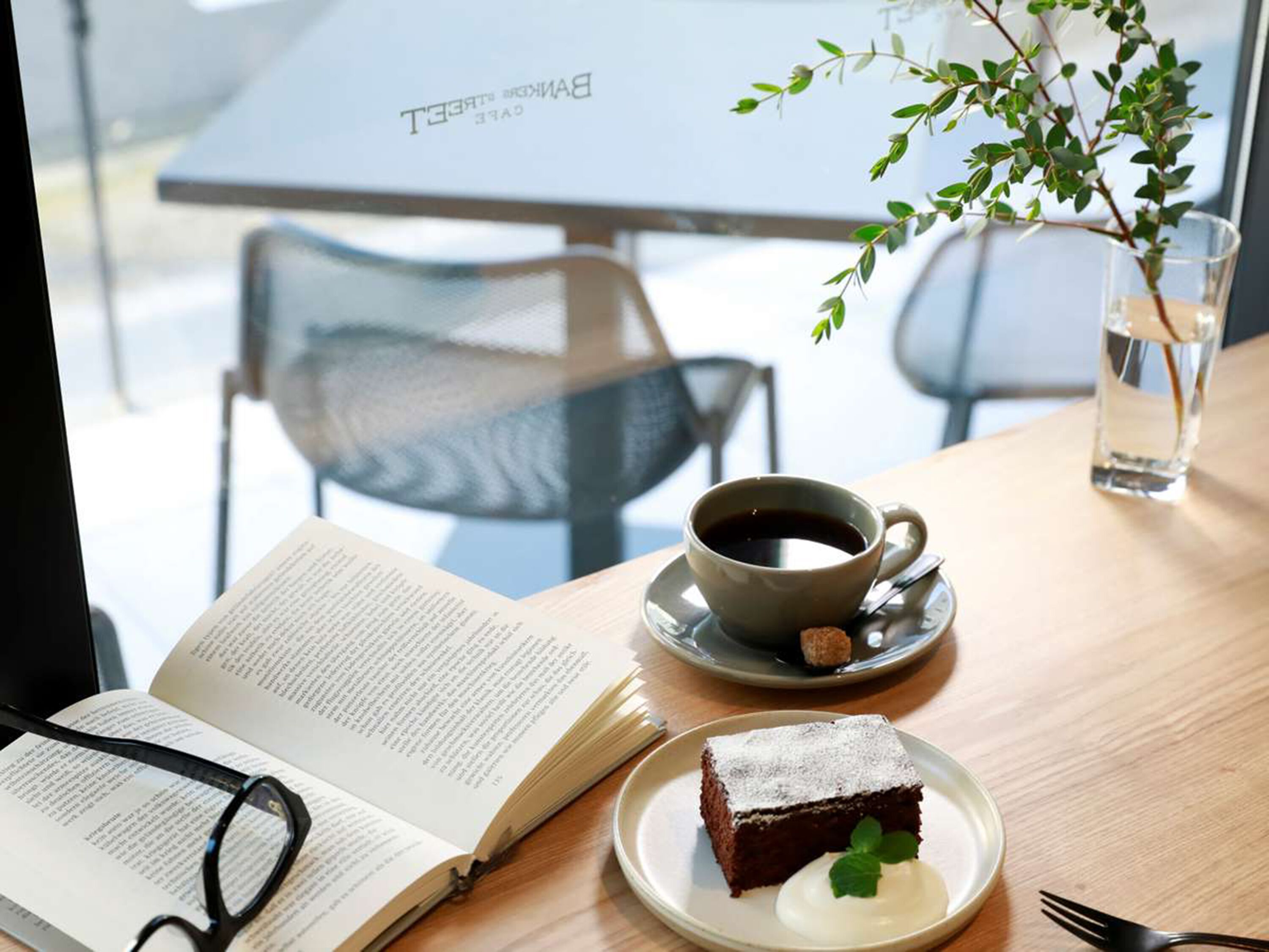 Une table avec un livre, une tasse de café, une part de gâteau et un verre d’eau.