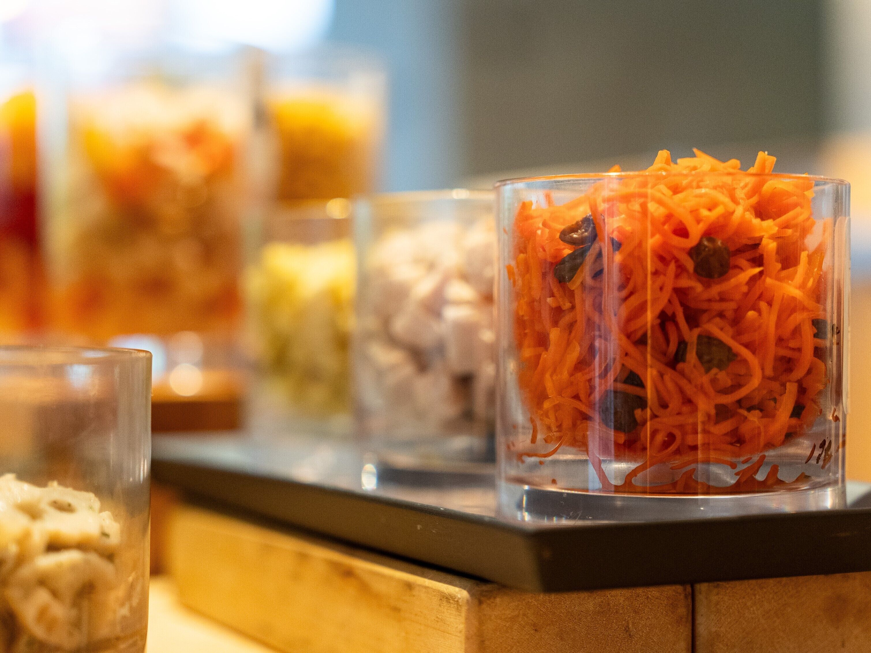 A buffet with various dishes, including a glass container with shredded carrots and other vegetables.