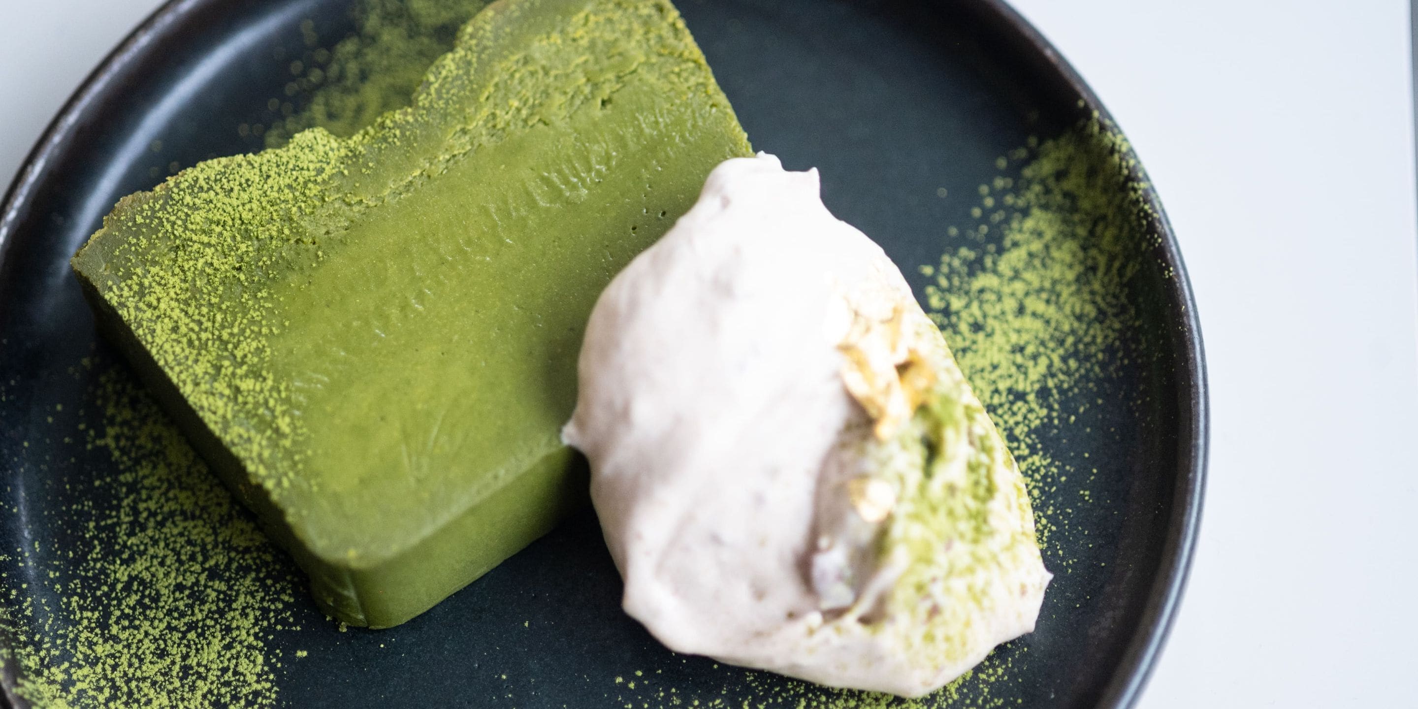 Un objeto rectangular verde y una porción de helado blanco sobre un plato negro.