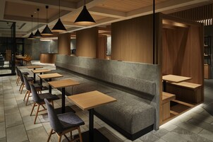Un interior de restaurante moderno con largas mesas de madera y bancos acolchados, iluminación colgante y una paleta de colores neutros.