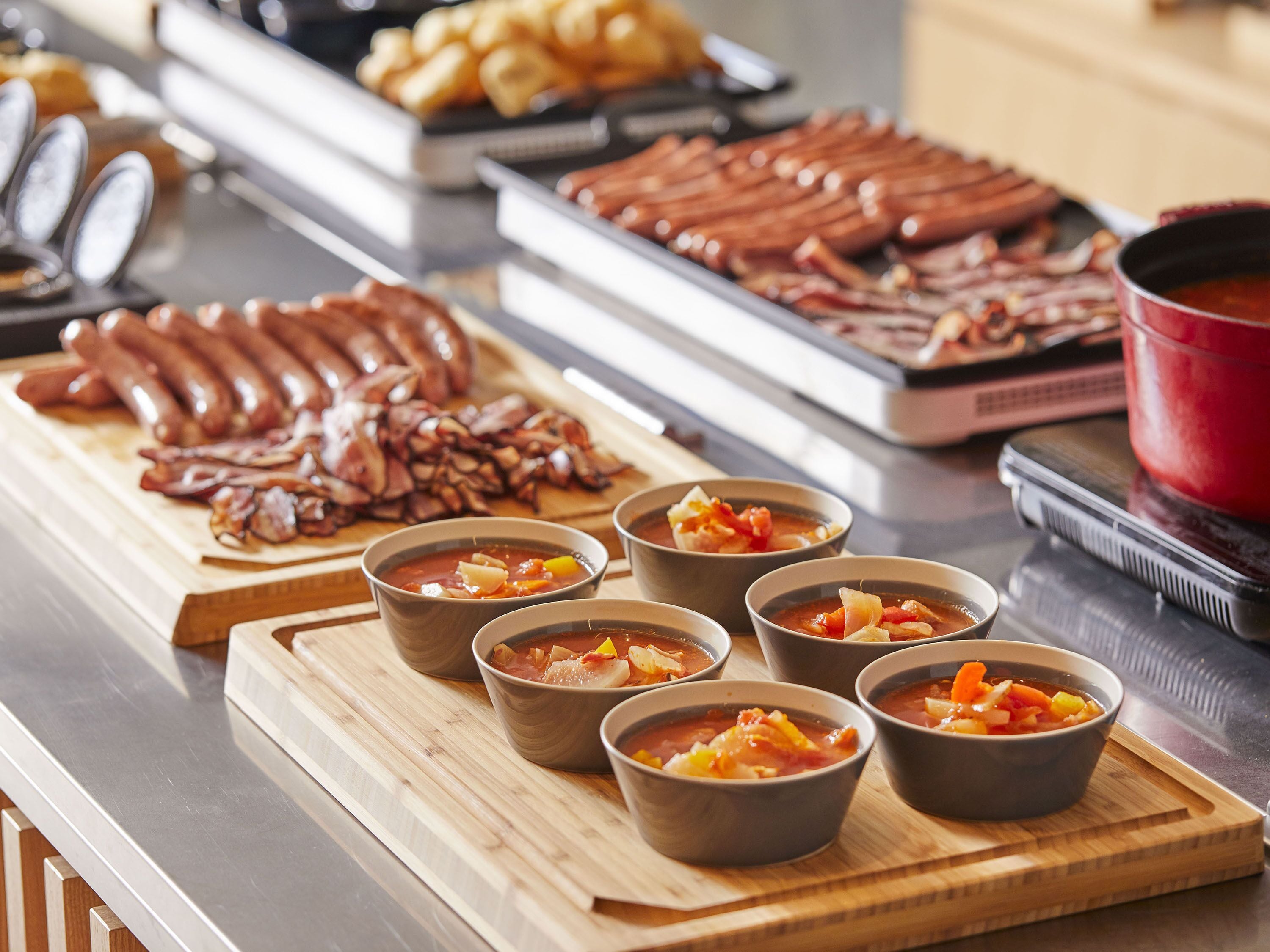 A buffet with various dishes including sausages, bacon, and bowls of soup.