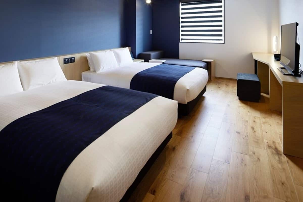 Una habitación de hotel con dos camas, un escritorio, una silla, un televisor y una ventana con persianas.