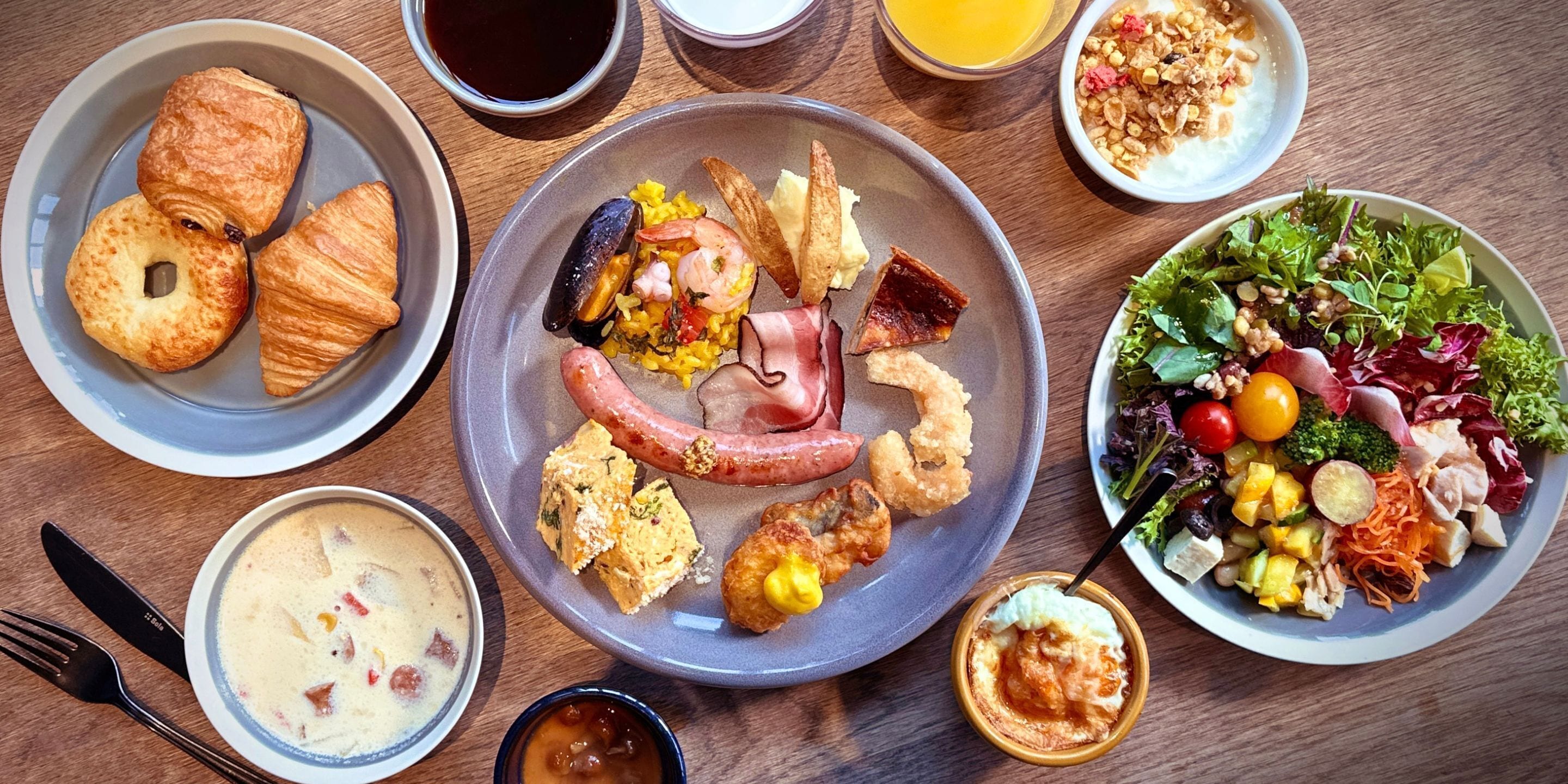 A variety of dishes including croissants, seafood, and a salad on a wooden table.