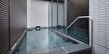 Un área de piscina interior moderna con barandillas de cristal y suelo de baldosas.