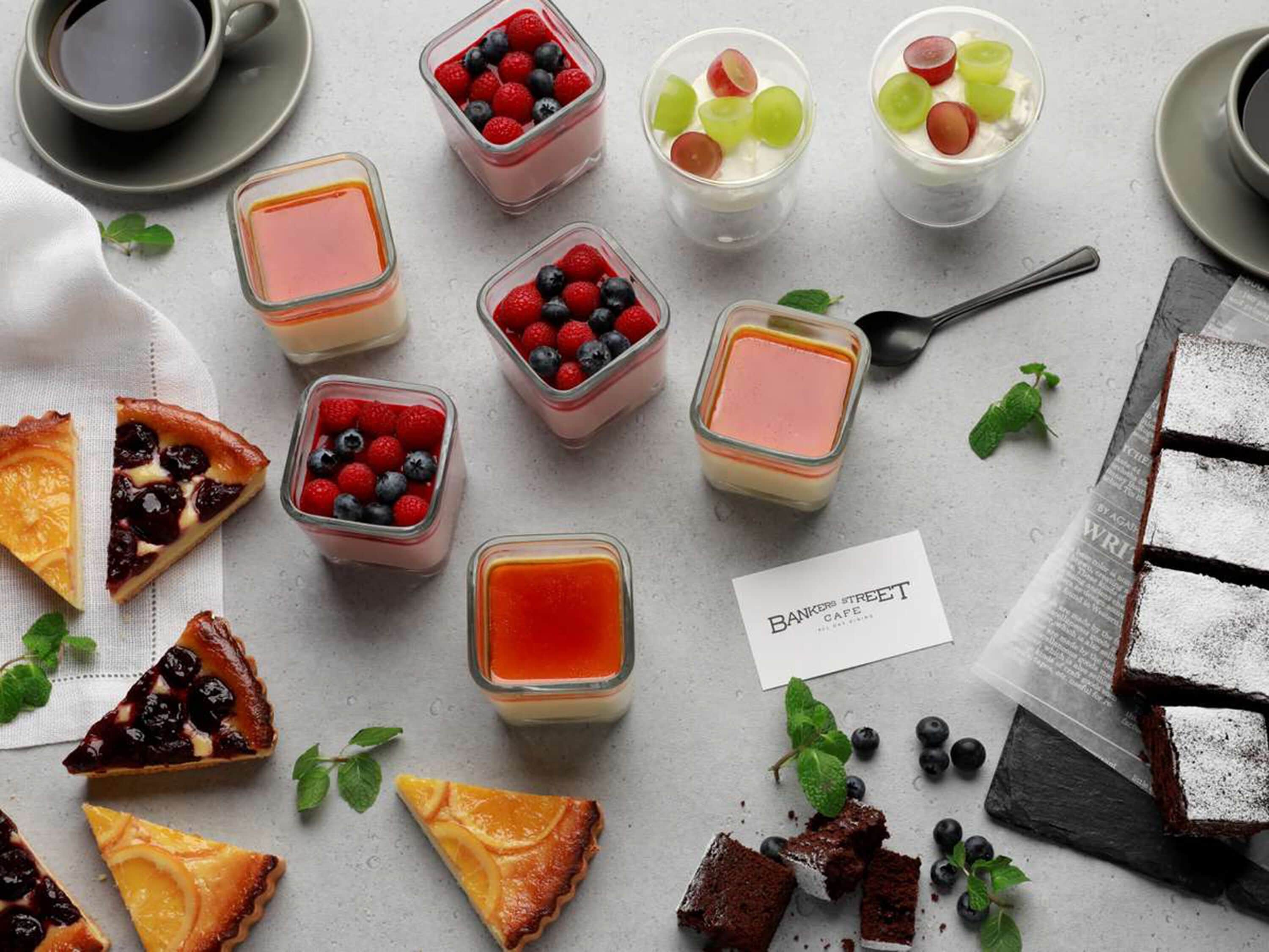 A variety of desserts including fruit tarts, panna cotta, and a cake with powdered sugar, arranged on a table with a menu card.