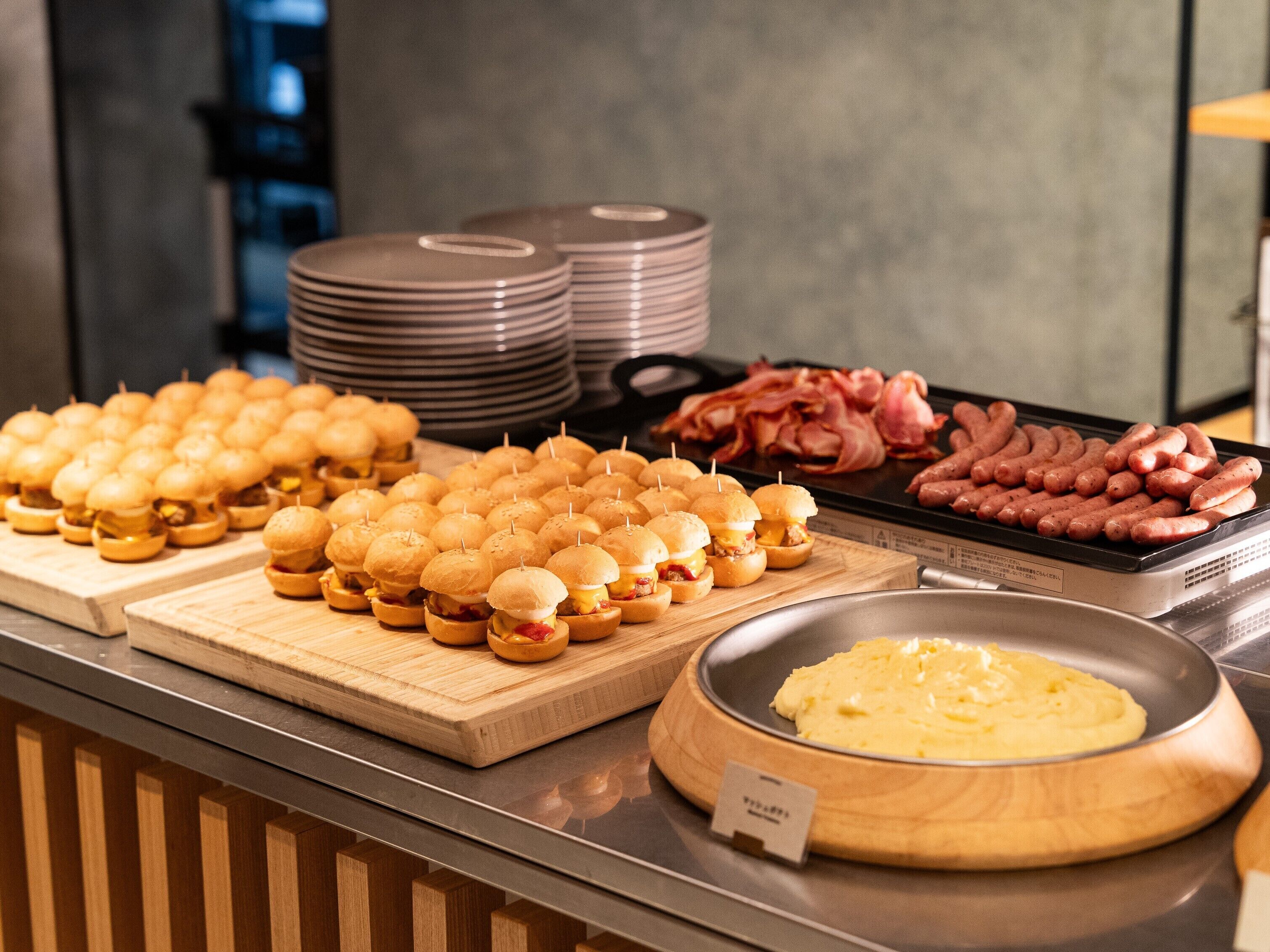 Un buffet con diversi piatti, tra cui mini panini, salsicce e una ciotola di purè di patate.