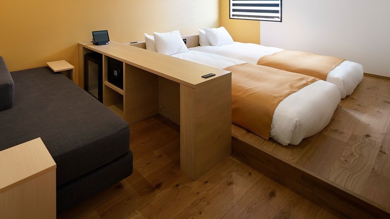 Une chambre d’hôtel de taille réduite, comprenant un lit, un bureau et un petit coin salon.