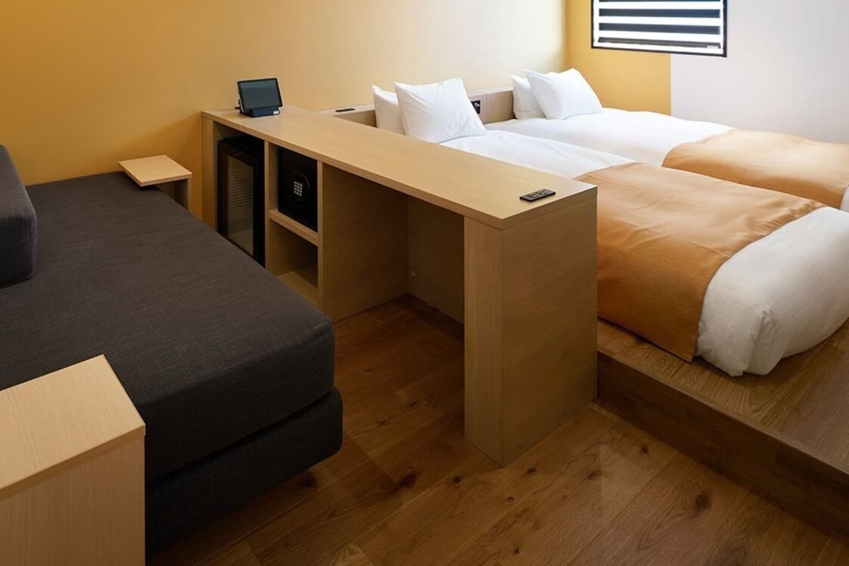 A compact hotel room with a bed, a desk, and a small seating area.