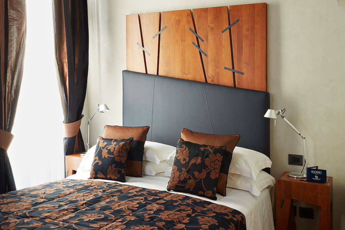 A hotel room with a large bed, two bedside tables, a nightstand, a wooden headboard, and a wall-mounted artwork.