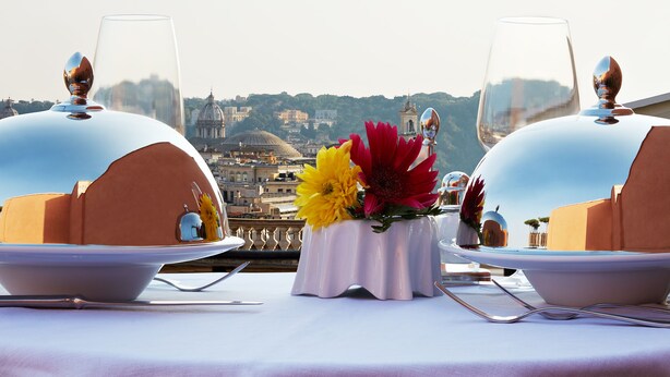 A table set with white tablecloths, two wine glasses, and a vase with yellow and red flowers. - The Code Hotel (Rome)