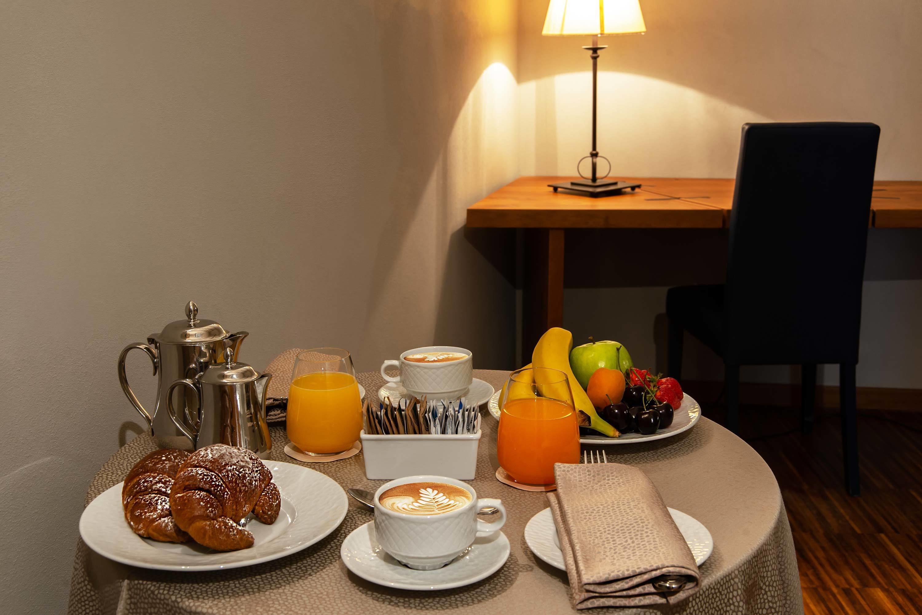A breakfast table with croissants, coffee, juice, and fruit.