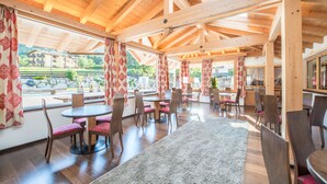 A spacious dining area with wooden beams, large windows, and red patterned curtains. - Hotel Alpenrose (Altopiano della Vigolana)