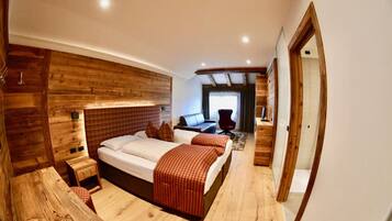 A wooden-themed bedroom with a bed, bedside tables, and a seating area.
