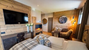 A cozy room with a fireplace, a flat-screen TV, a sofa, and a chair. - Hotel Alpenrose (Altopiano della Vigolana)