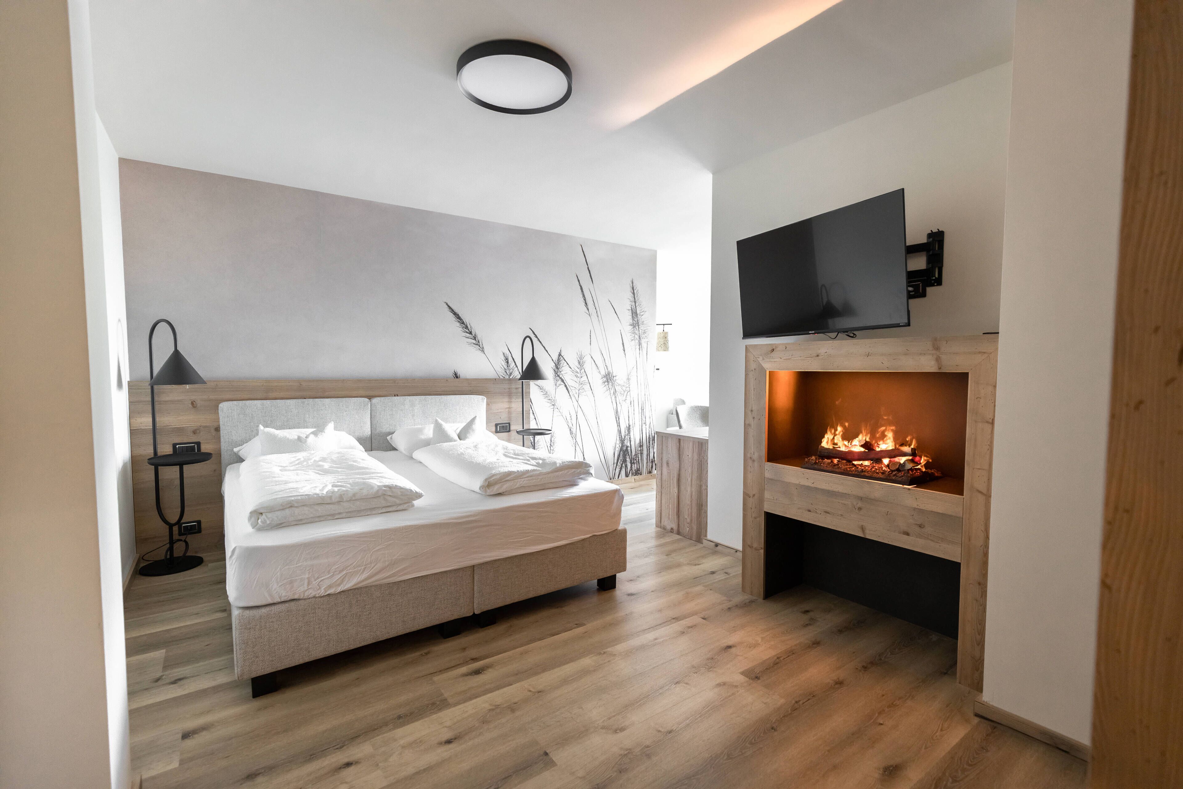 A modern bedroom with a large bed, a fireplace, and a mounted TV.