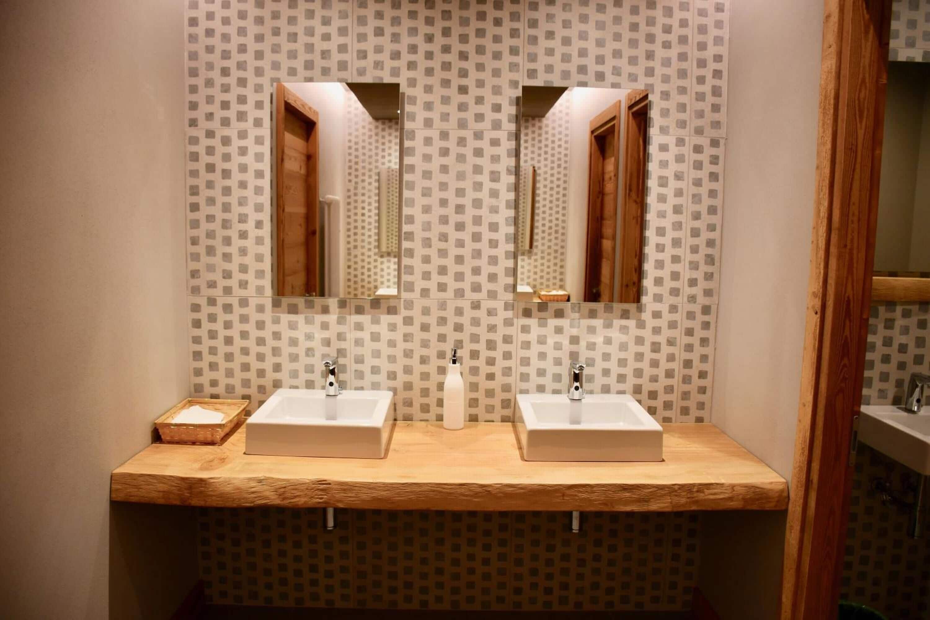 A bathroom with two sinks, wooden vanity, patterned wallpaper, and mirrors.