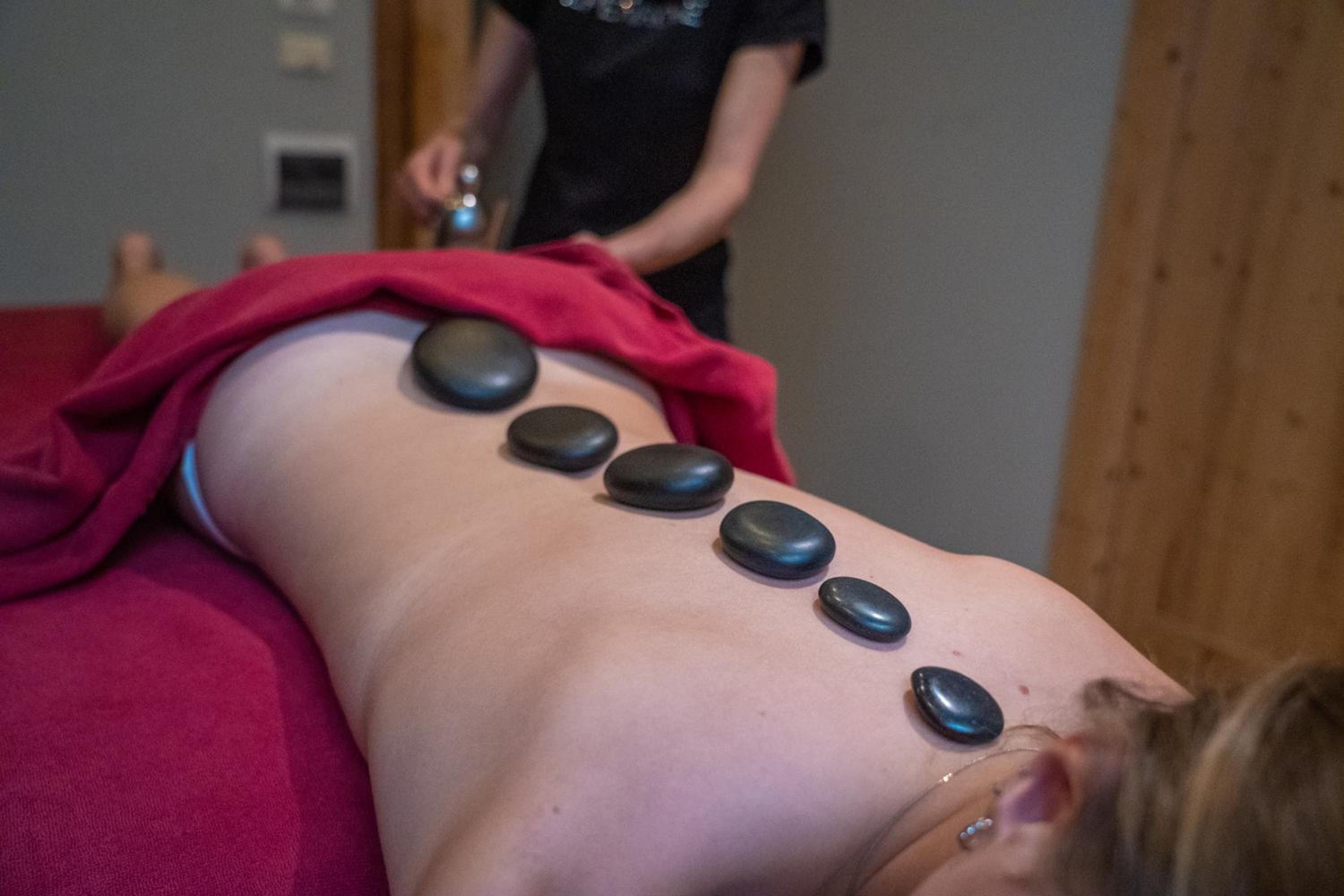 Eine Person erhält eine Steinmassage, wobei fünf Steine auf dem Rücken platziert sind.