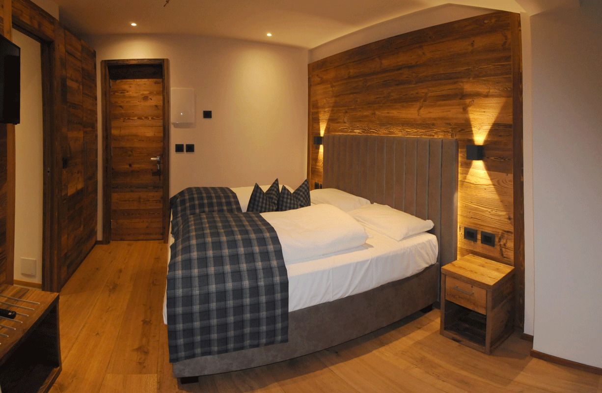 Una camera da letto con testiera in legno, un letto con coperta a quadri, un comodino e un tavolino notte con una lampada.