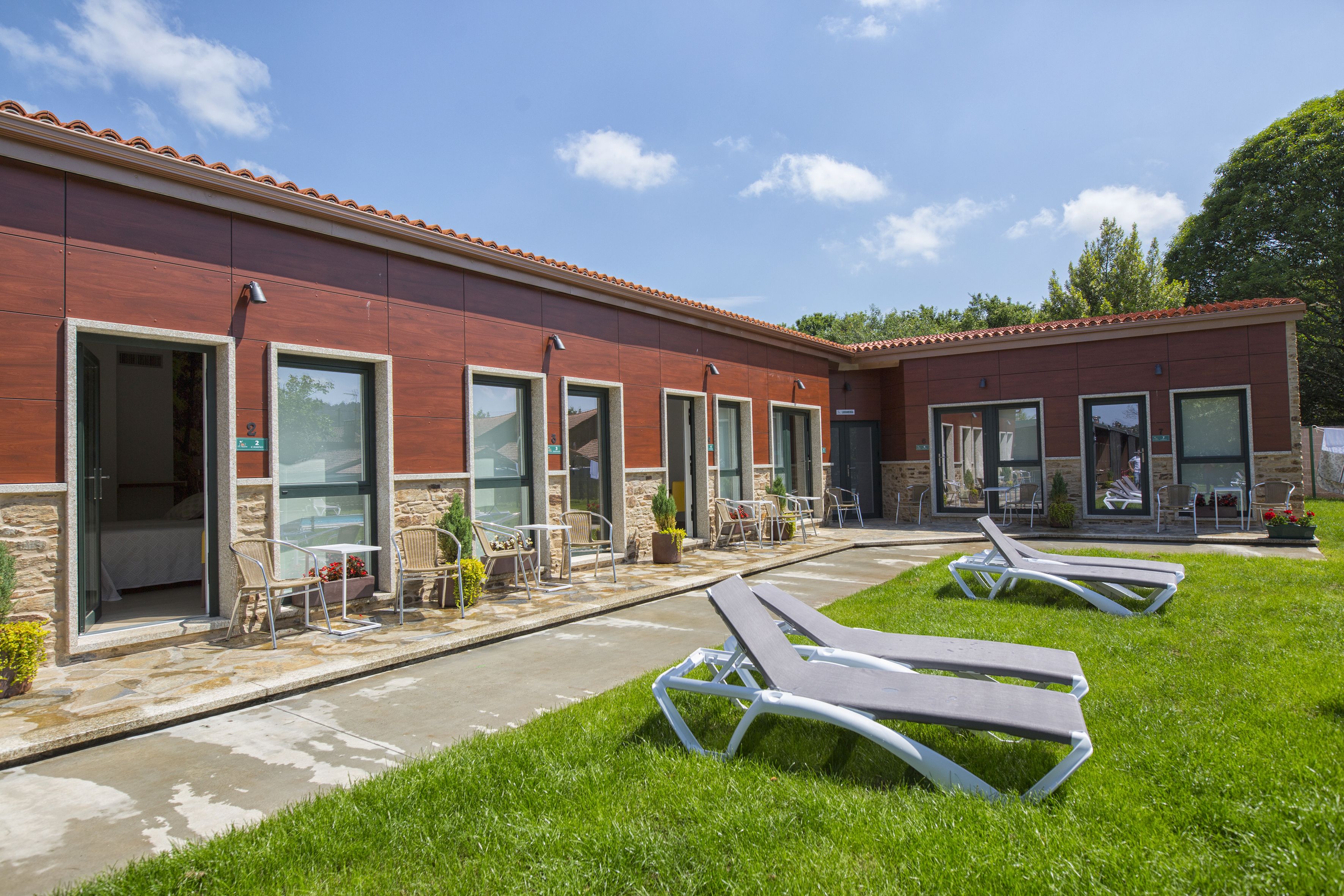 A building with multiple rooms, outdoor seating, and a grassy area with lounge chairs.