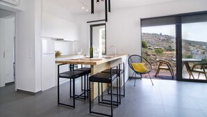 Une cuisine moderne dotée d’un îlot central, de tabourets de bar noirs et offrant une vue sur une colline grâce à de grandes fenêtres.