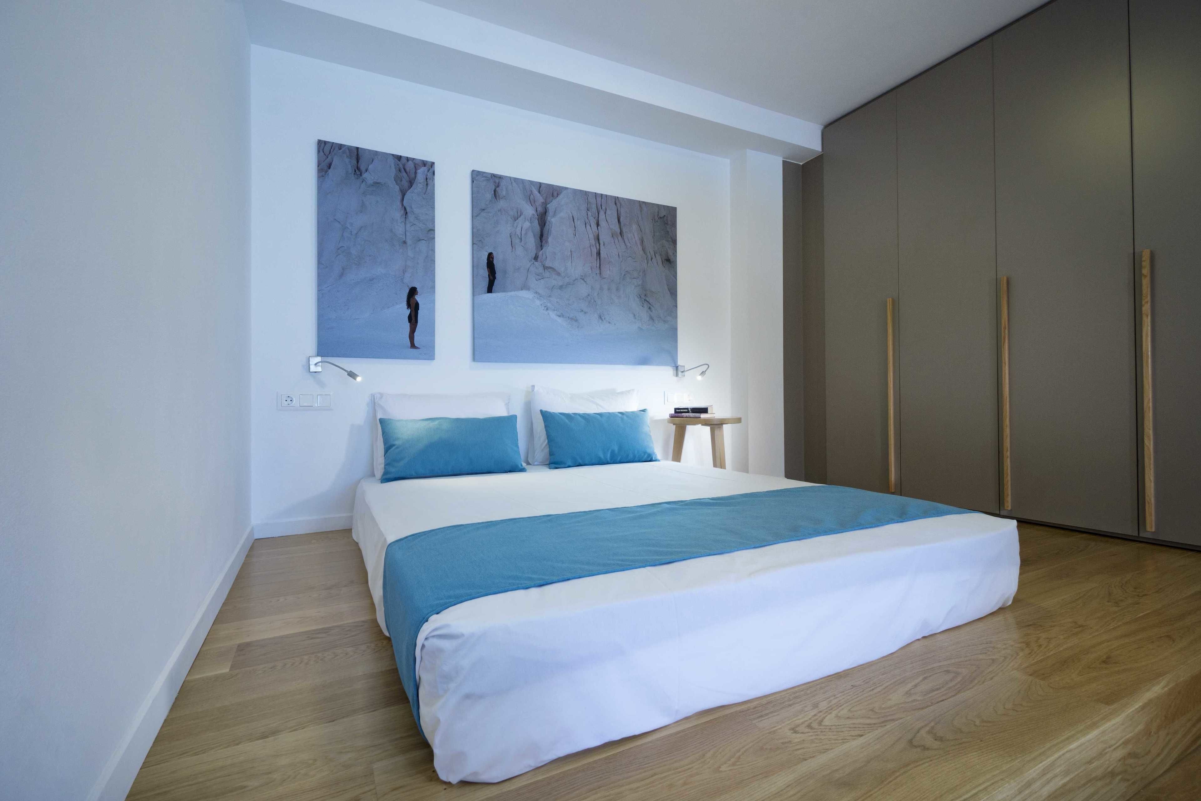 A modern bedroom with a large bed, two wall-mounted artworks, a bedside table, and a wardrobe.