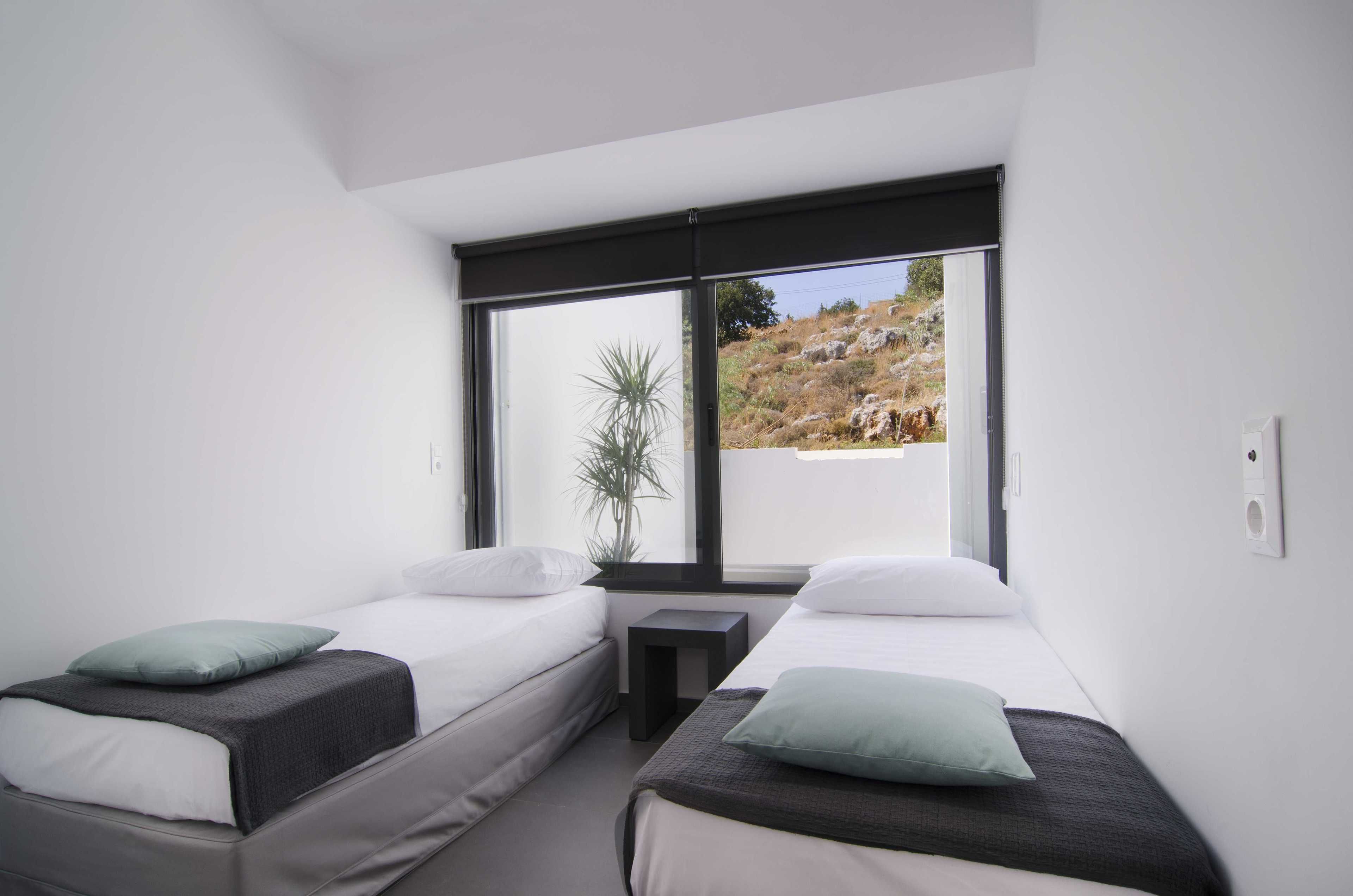A modern bedroom with two single beds, a small table, and a large window offering a view of a rocky landscape.