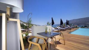 Une terrasse en bois avec une table et des chaises, une piscine et des chaises longues avec des parasols.