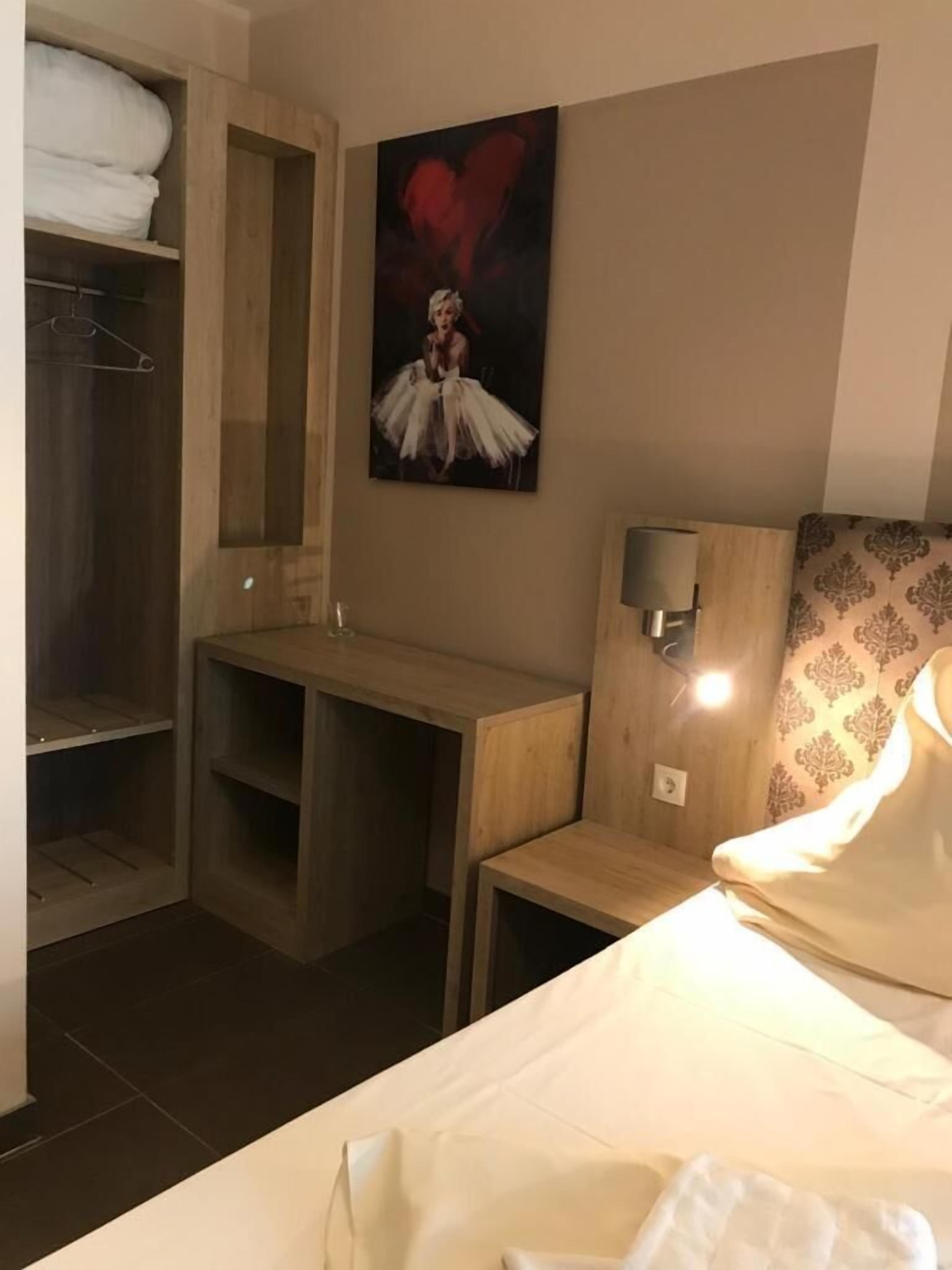 Et hotelværelse med seng, skrivebord, garderobeskab og et billede på væggen.