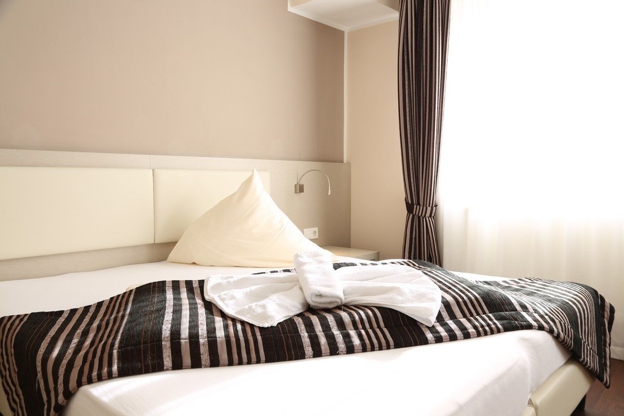 A hotel room with a bed, a headboard, a nightstand, a lamp, and a window with curtains.
