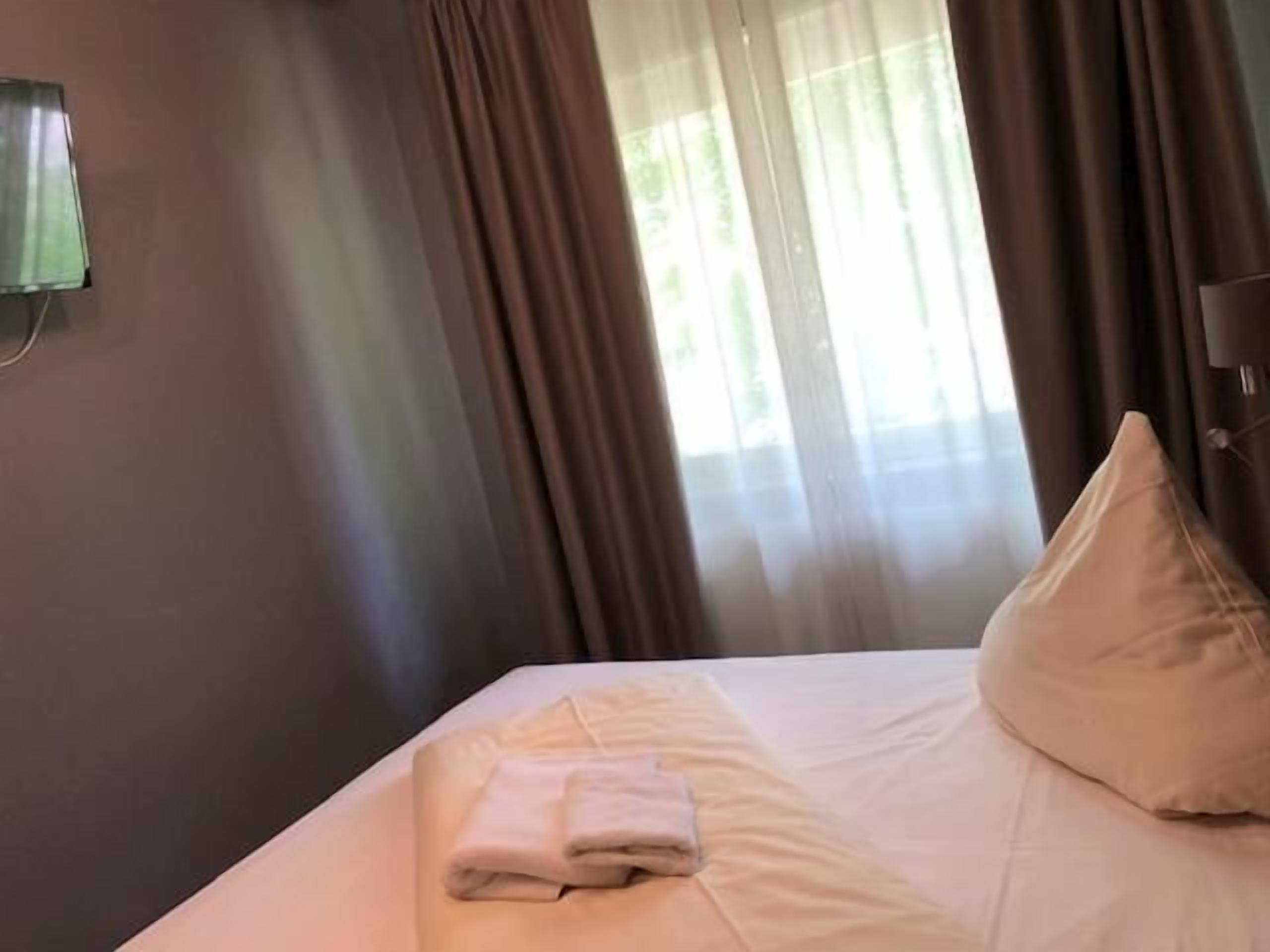 A neatly made bed with a folded towel, a pillow, and a wall-mounted lamp.