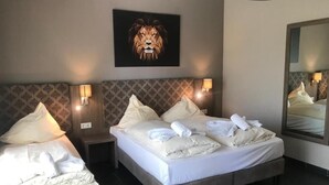 Una habitació d'hotel amb un llit gran, un panell de capçalera amb una pintura de lleó, dues làmpades de nit i un mirall a la paret.