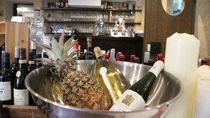 Zona de bar amb un bol metàl·lic que conté una pinya, ampolles de vi i una espelma.