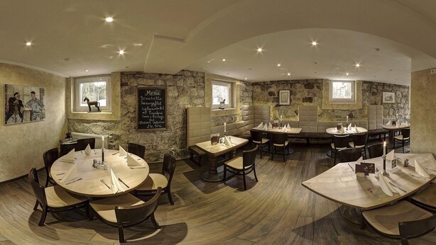 Un restaurant amb taules rodones, seients tapissats, parets de pedra i quadres emmarcats.