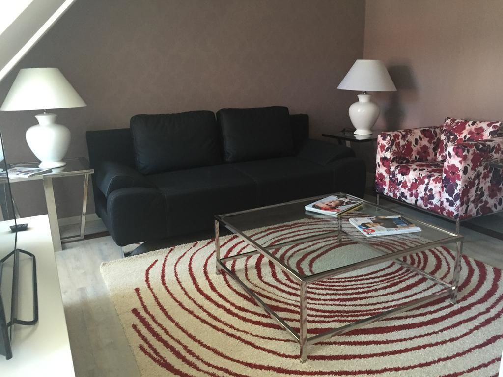 A living room with a black sofa, a floral sofa, a glass coffee table, and two lamps.