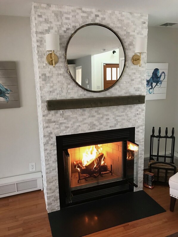 Una chimenea con un revestimiento de ladrillo blanco, un espejo redondo encima y una lámpara de pared.
