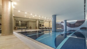 Une piscine intérieure moderne, avec de l’eau cristalline, entourée de piliers de couleur beige et dotée d’un sol carrelé.