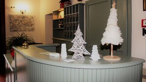 Bancada de recepção com árvore de Natal branca, uma  árvore pequena e branca, e um sino em uma prateleira.