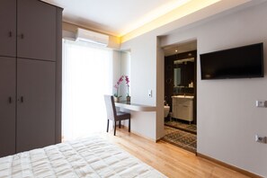 A bedroom with a bed, a desk, a chair, a TV, and a bathroom visible through an open door. - Deluxe 2 bdrm apartment in Voula (Voula)