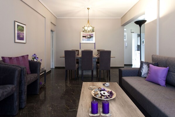 A modern living room with a dining area, featuring a chandelier, a sofa, and a coffee table with decorative items. - Deluxe 2 bdrm apartment in Voula (Voula)
