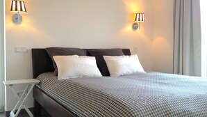 A neatly made bed with a patterned bedspread, two white pillows, and two wall-mounted lamps. - Quiet 5* vacation home right on the water | WLAN | sauna | fireplace | whirlpool tub (Kosel / Schlei)