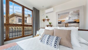 Une chambre d’hôtel avec un lit, une fenêtre donnant sur des immeubles, un climatiseur fixé au mur et un tableau.