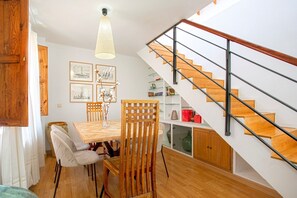Een eethoek met een houten tafel en stoelen, een trap met glazen balustrade en ingelijste foto's aan de muur.