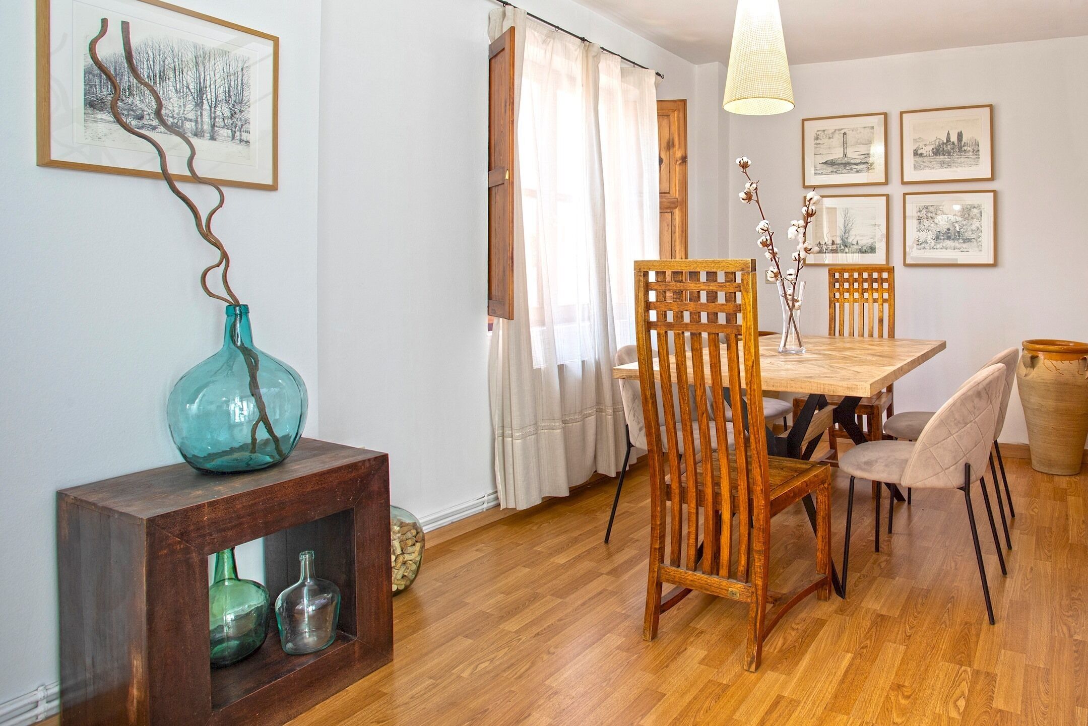 A dining area with a wooden table and chairs, a vase on a wooden console, and framed pictures on the wall.