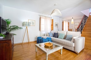Ein Wohnzimmer mit einer Couch, einem Couchtisch, einer Lampe, einem Fernseher und einer Treppe.