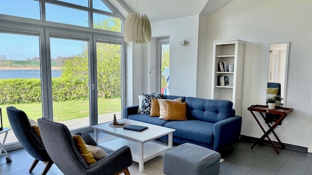 Een moderne woonkamer met een blauwe bank, twee fauteuils, een salontafel en een boekenkast.