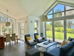 A modern living room with a large window, a dining area, and a sofa set.