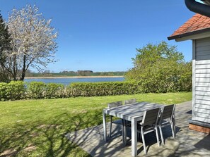 A patio with a table and chairs, a view of a lake, and a building with a red roof.