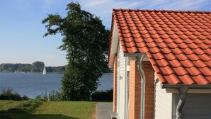 A house with a red-tiled roof, a brick exterior, and a view of a lake with a sailboat. - Holiday house in direct water situation | Sauna | Whirlpool | Fireplace | Free Wi-Fi (Kosel)