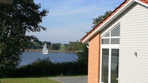 A house with a brick exterior and large windows, overlooking a lake with a sailboat. - Holiday house in direct water situation | Sauna | Whirlpool | Fireplace | Free Wi-Fi (Kosel)